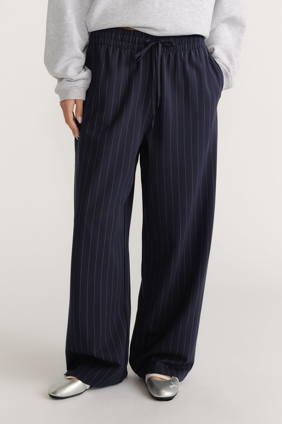 Woman wearing navy pinstripe wide-leg pants with an elastic waist, styled casually with a grey sweatshirt and silver flats