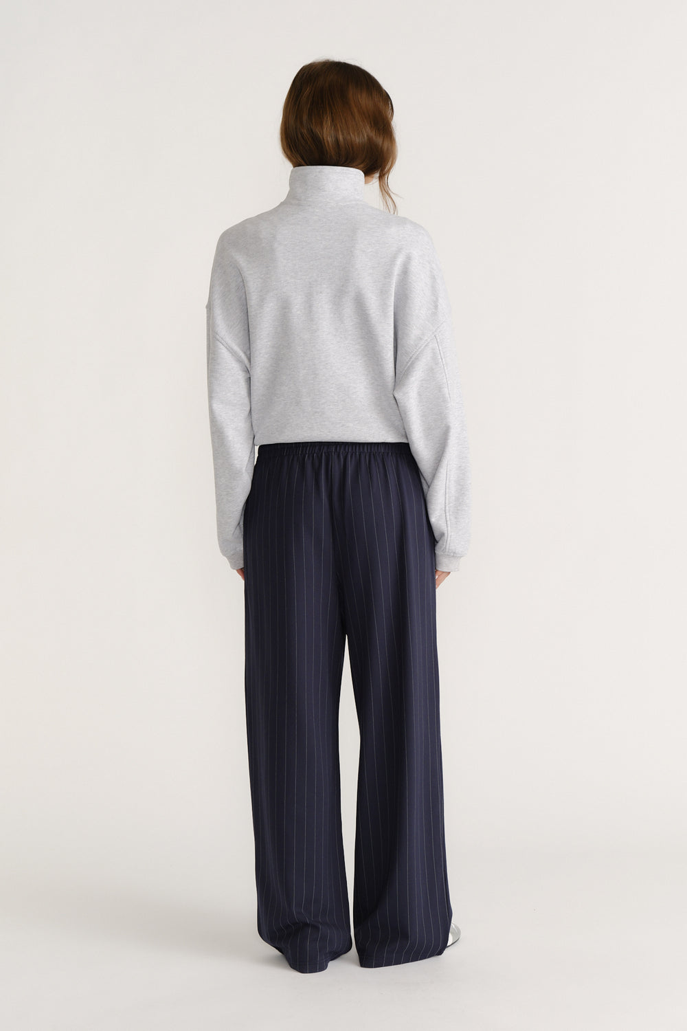 Woman seen from behind wearing navy pinstripe wide-leg pants paired with a light grey high-neck pullover