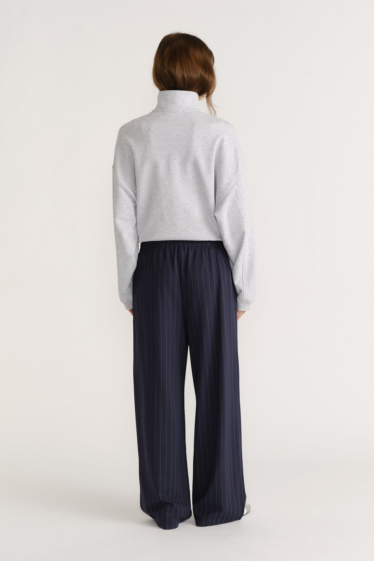 Woman seen from behind wearing navy pinstripe wide-leg pants paired with a light grey high-neck pullover