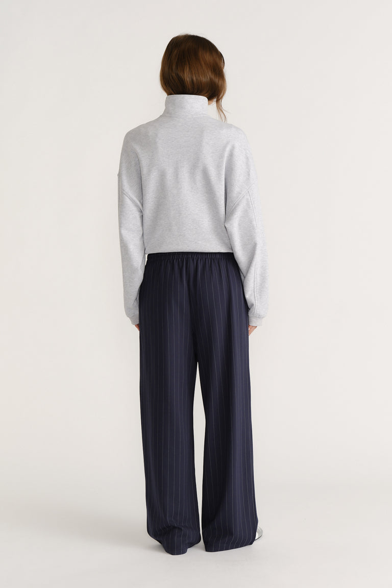 Woman seen from behind wearing navy pinstripe wide-leg pants paired with a light grey high-neck pullover