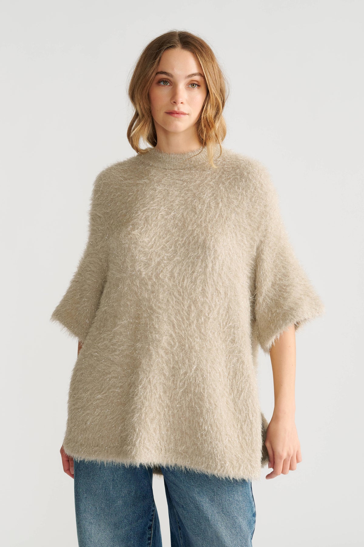 Woman wearing a soft biscuit-toned oversized knit top with textured short sleeves paired with relaxed blue jeans.