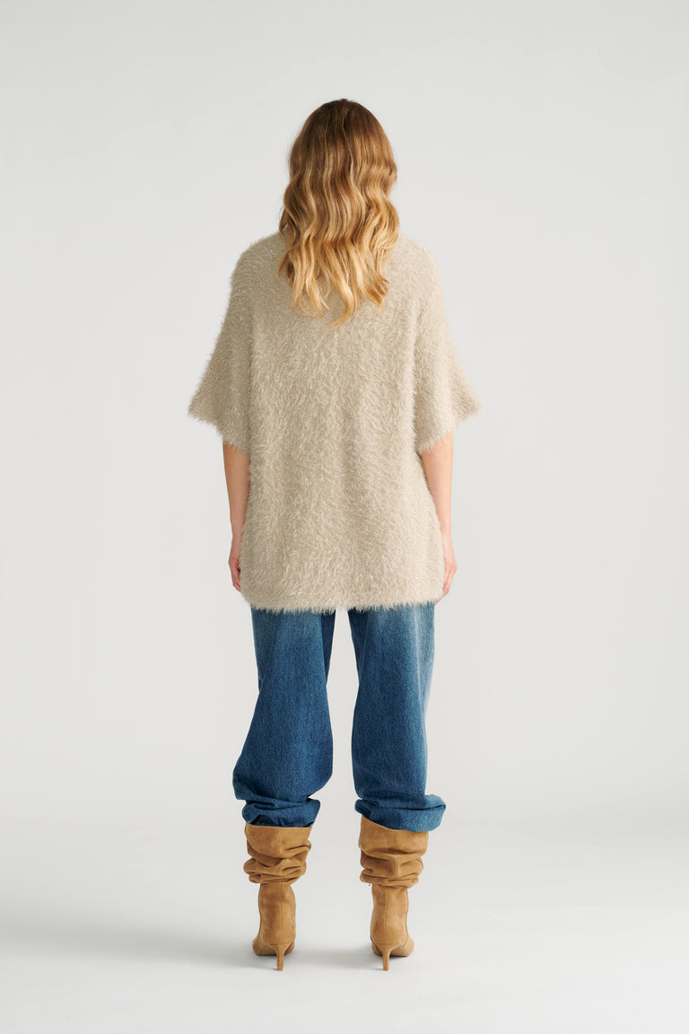 Woman wearing a relaxed biscuit-colored oversized knit tee paired with loose blue jeans and slouchy tan boots, back view.