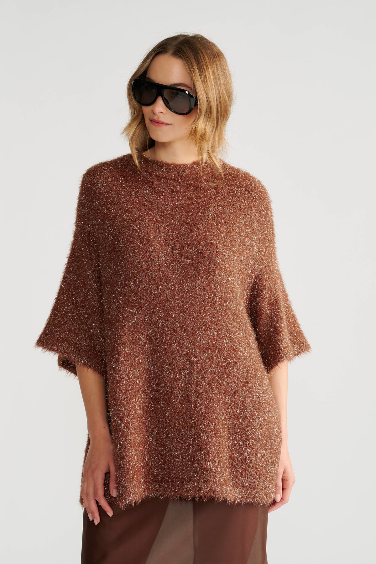 Woman wearing a relaxed oversized knit tee in warm rust with textured fabric and elbow-length sleeves paired with sunglasses.