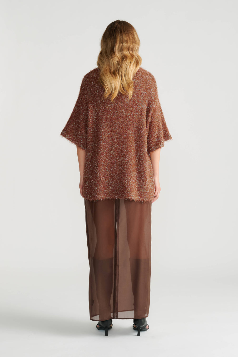 Back view of woman wearing a textured oversized rust knit tee paired with a sheer brown maxi skirt and black heels.