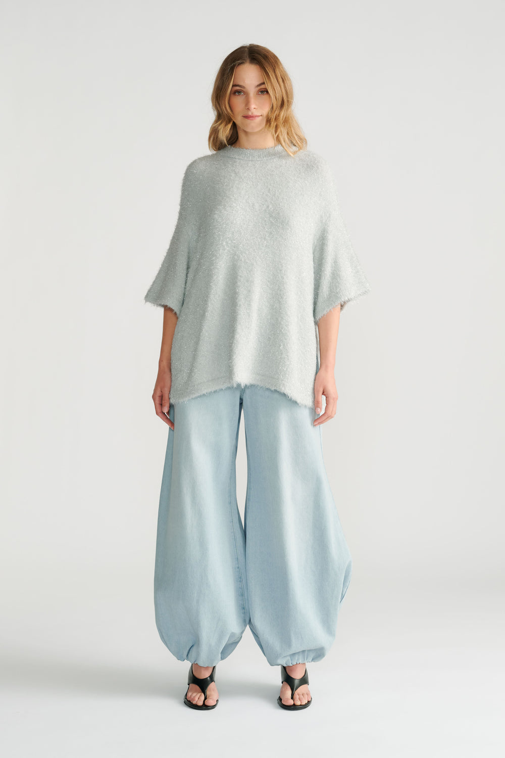 Soft light grey oversized knit tee paired with wide-leg, balloon-style light denim pants and black open-toe sandals.