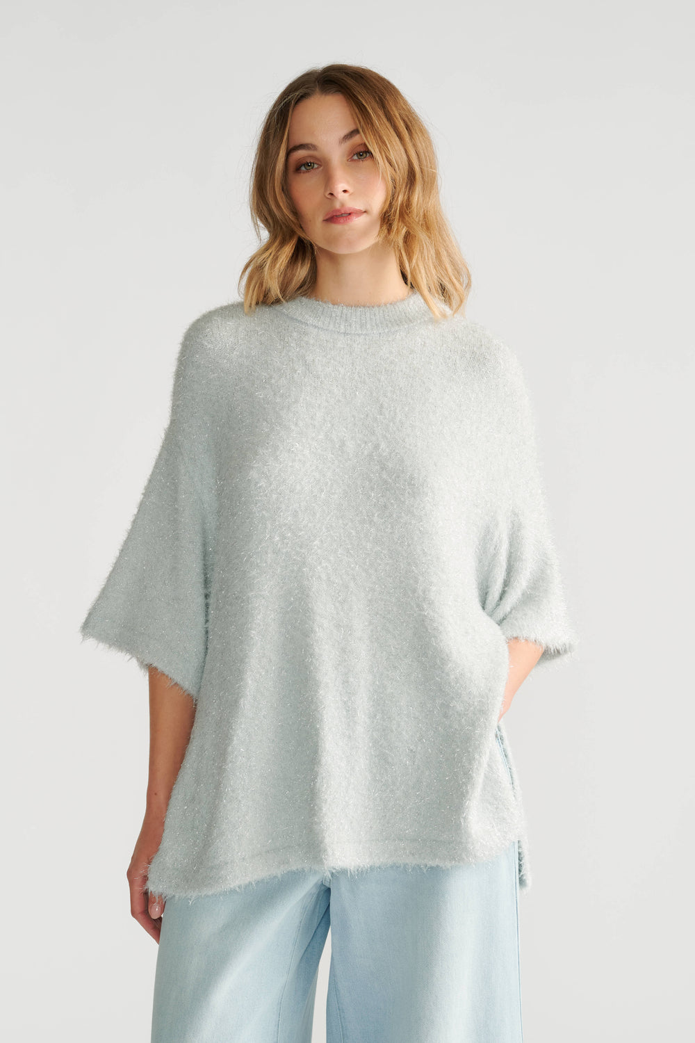 Woman wearing a soft, oversized light grey knit tee with short sleeves paired with loose light blue pants.
