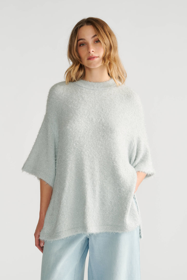 Woman wearing a soft, oversized light grey knit tee with short sleeves paired with loose light blue pants.