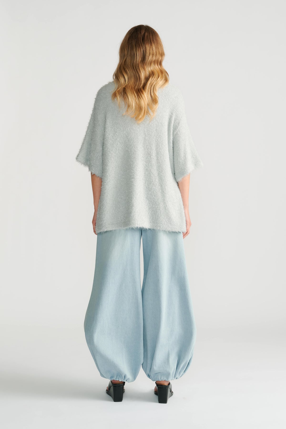 Back view of woman wearing a soft oversized knit top paired with light blue wide-leg balloon jeans and black heels.