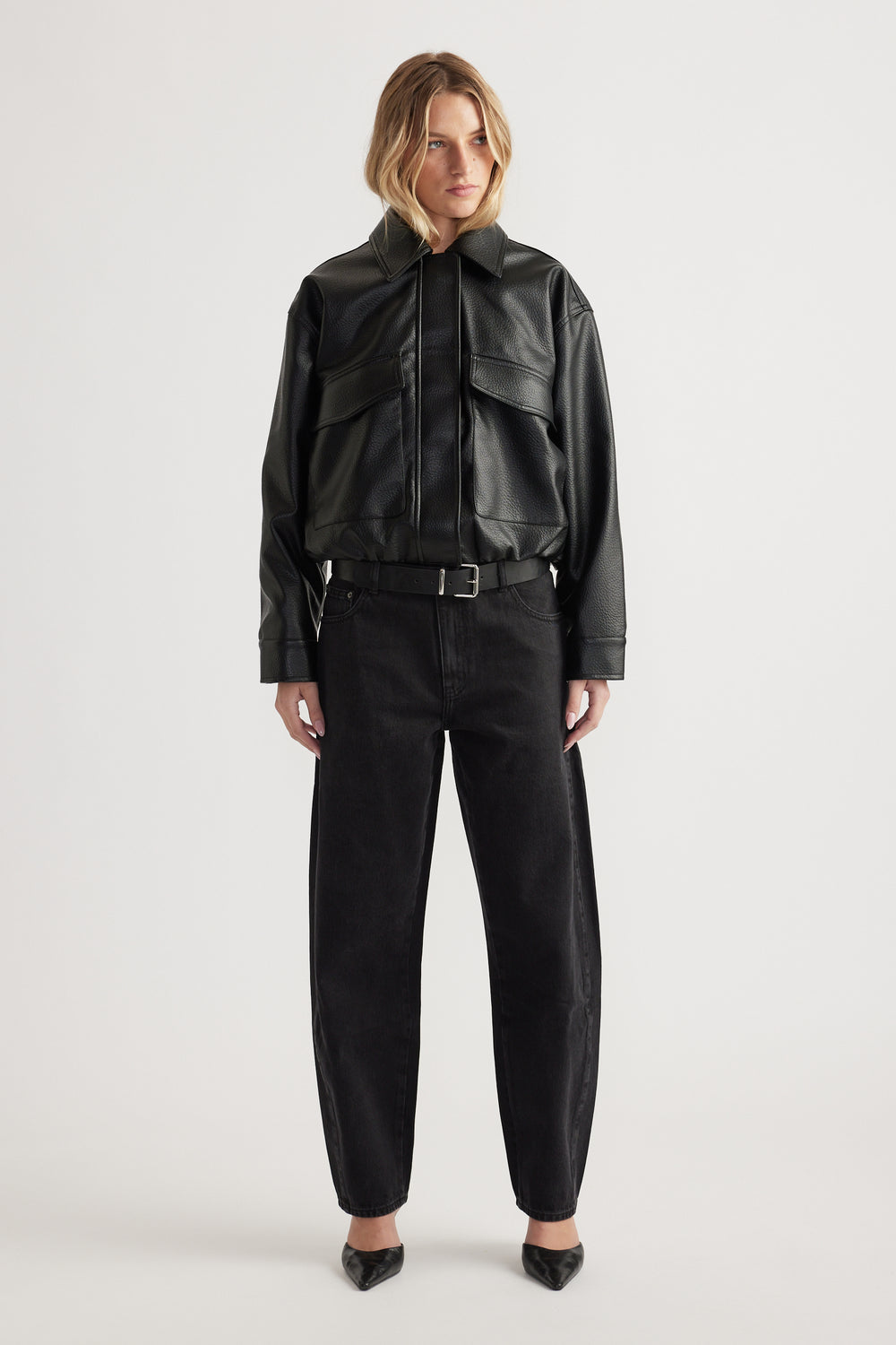 Woman wearing relaxed black jeans paired with a cropped belted faux leather jacket and pointed black heels