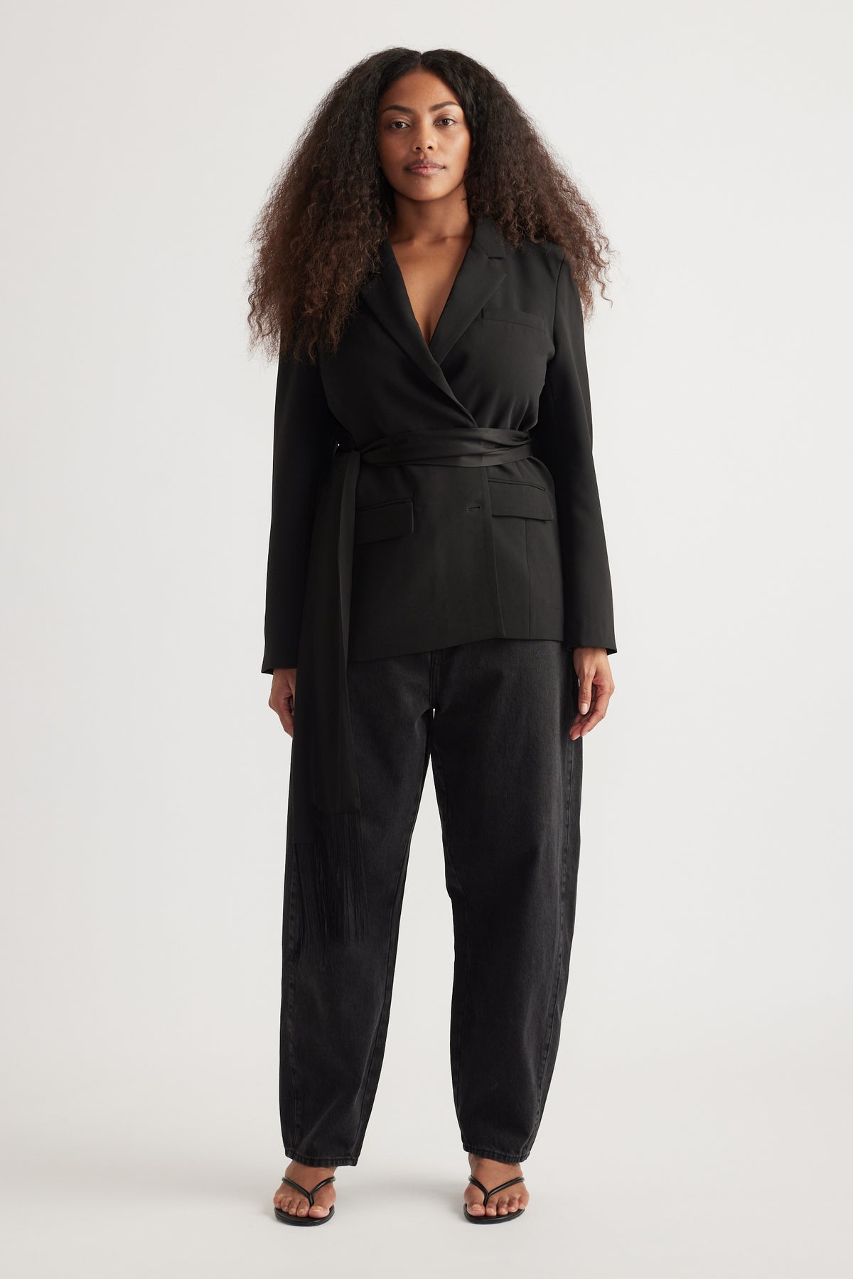 Woman wearing a black wrap blazer with matching tapered barrel-leg jeans and strappy sandals