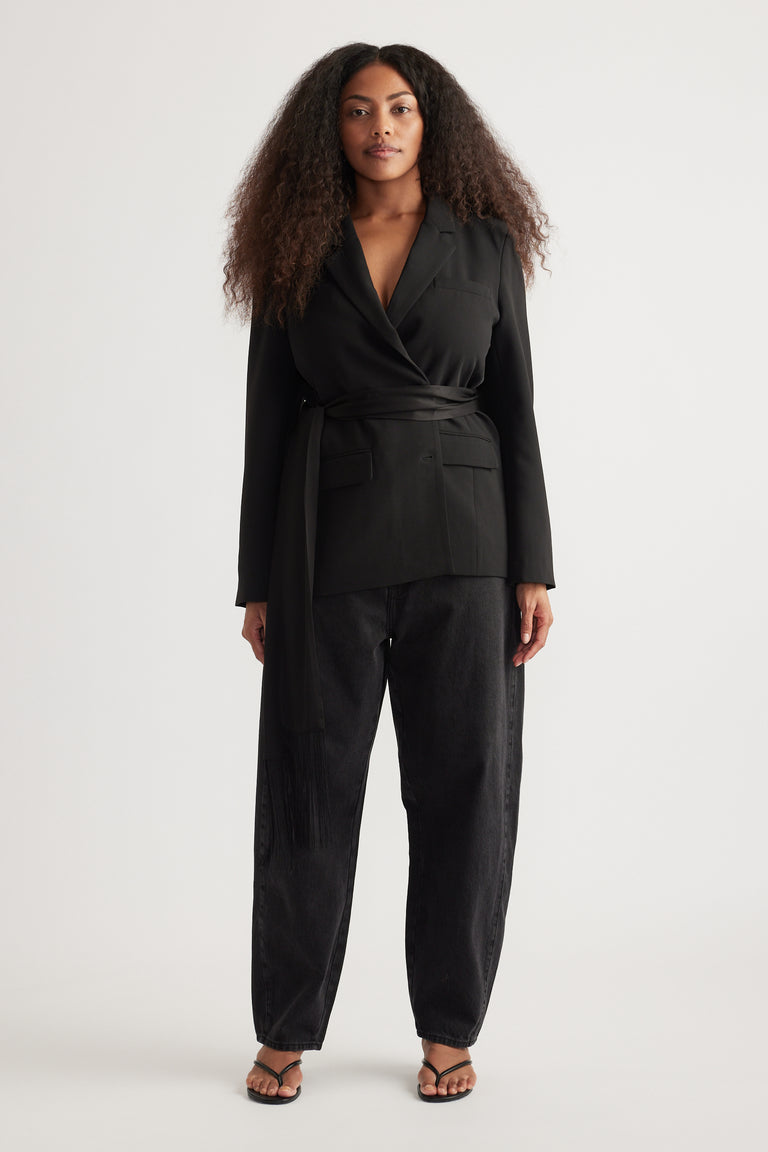 Woman wearing a black wrap blazer with matching tapered barrel-leg jeans and strappy sandals