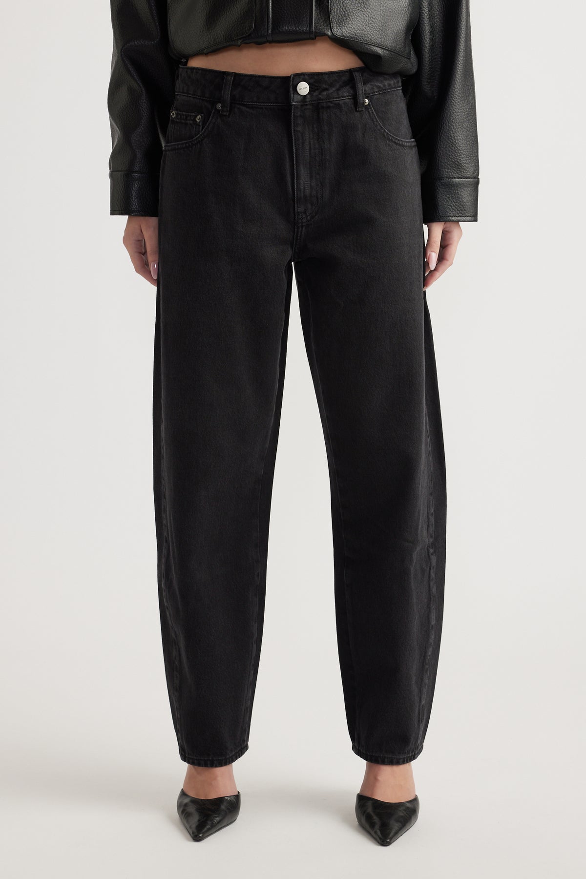 Front view of black barrel leg jeans paired with pointed black heels and a cropped jacket