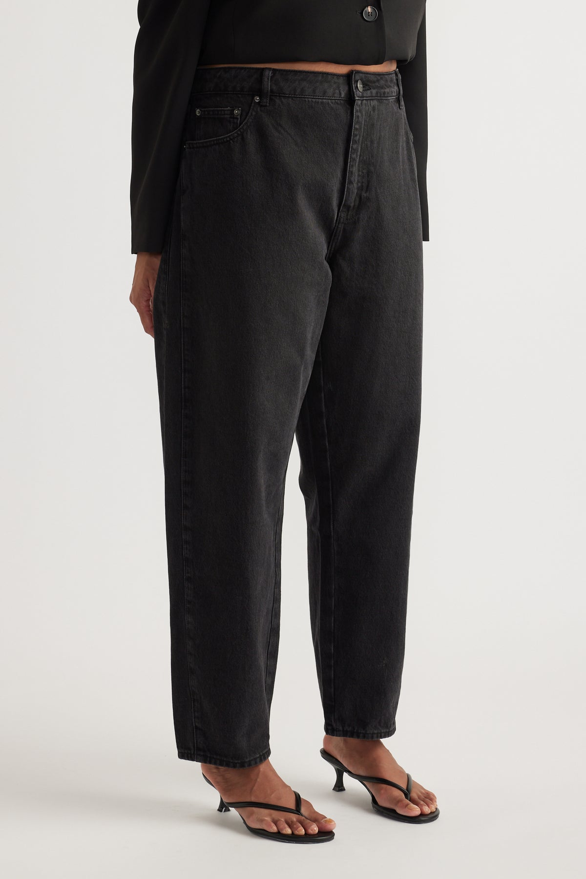 Woman wearing high rise charcoal barrel leg jeans with a black blazer and strappy heeled sandals