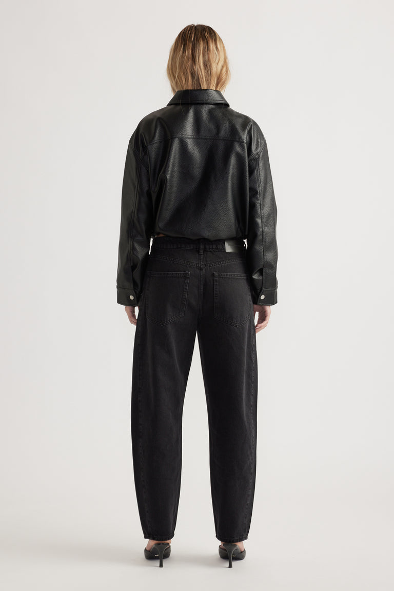 Woman wearing black barrel leg jeans paired with a cropped faux leather jacket and black heels, shown from behind