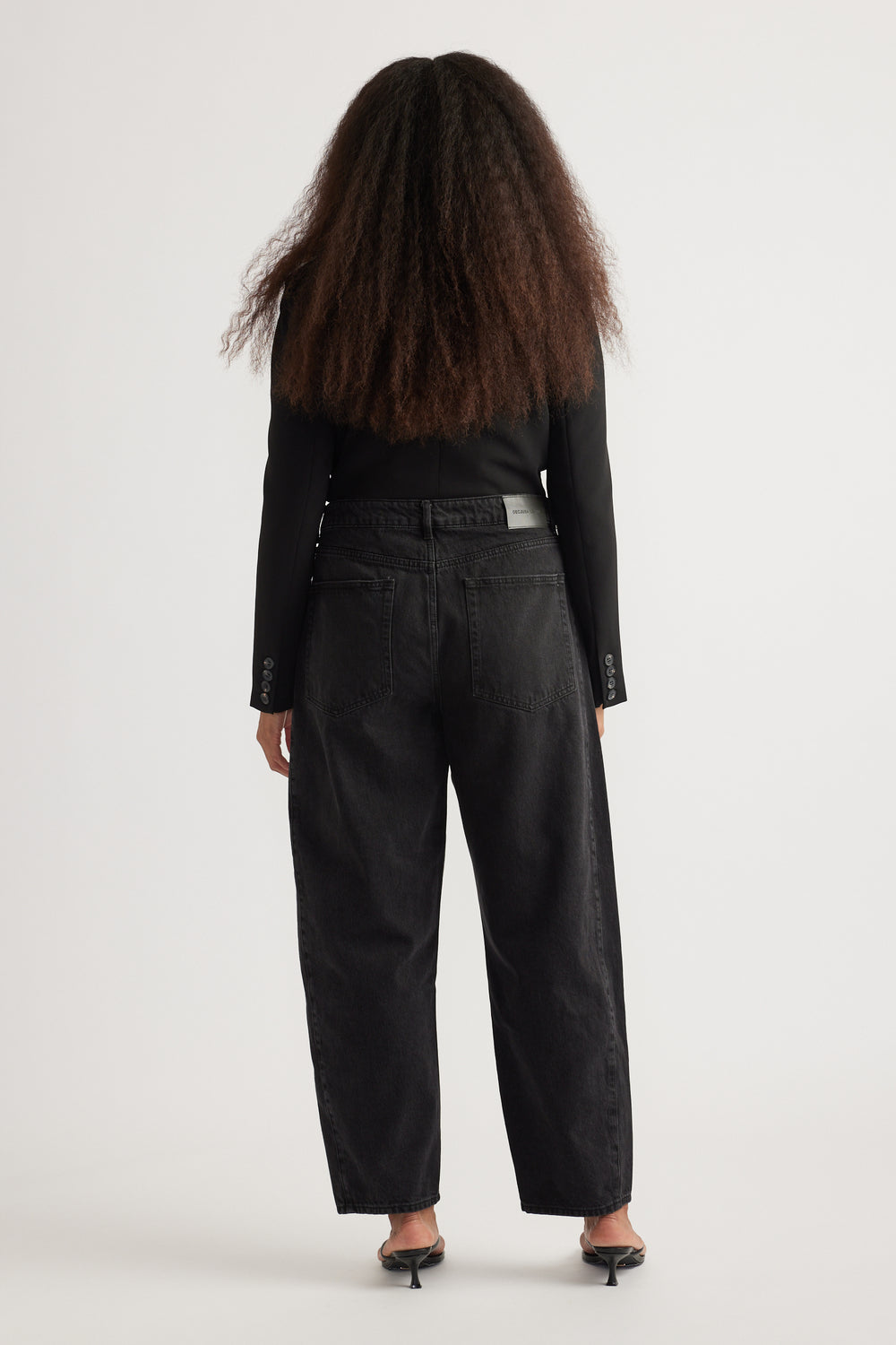 Back view of woman wearing black high rise barrel leg jeans with tapered ankles and a black long sleeve top
