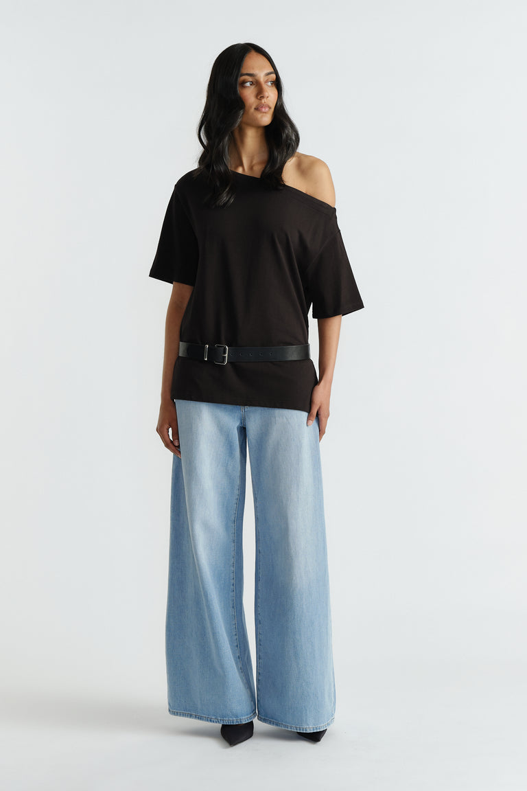 Woman wearing relaxed black off-shoulder tee with black belt, paired with light blue wide-leg denim jeans and black shoes.