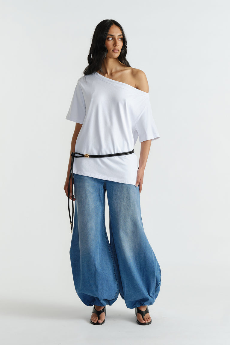 Woman wearing an off-shoulder white relaxed tee paired with voluminous wide-leg blue denim jeans and black belt