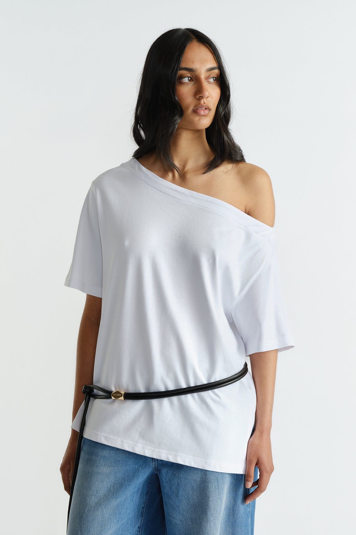 Woman wearing a relaxed white drop shoulder tee styled off one shoulder with wide-leg denim and a black belt accessory