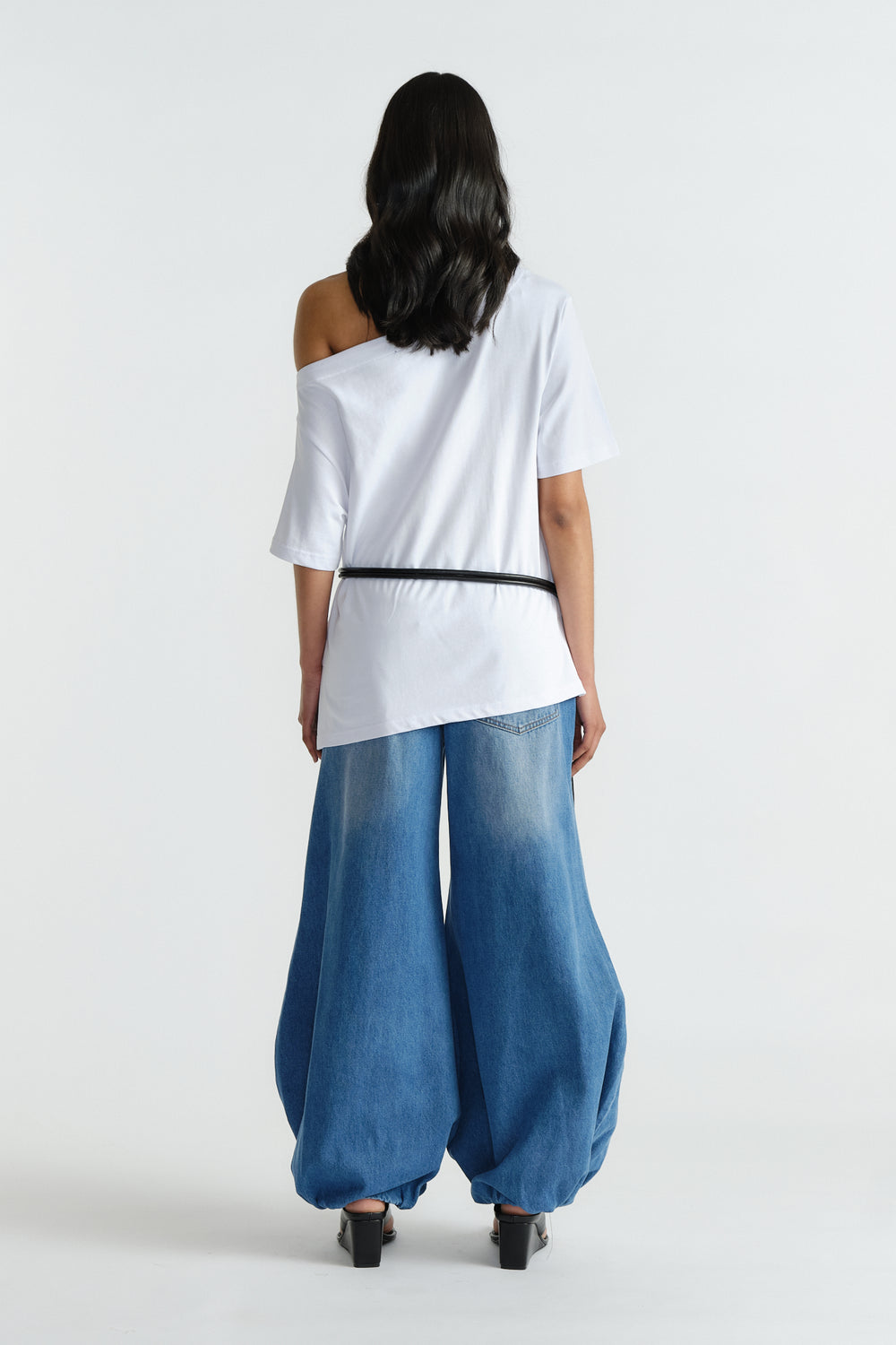 Woman wearing a white drop shoulder tee tucked into wide-leg, balloon-style blue denim jeans and black heels, seen from back