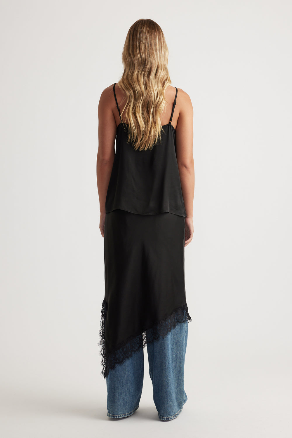 Woman wearing a black lace-trim cami layered over relaxed blue wide-leg denim jeans for a modern casual look.