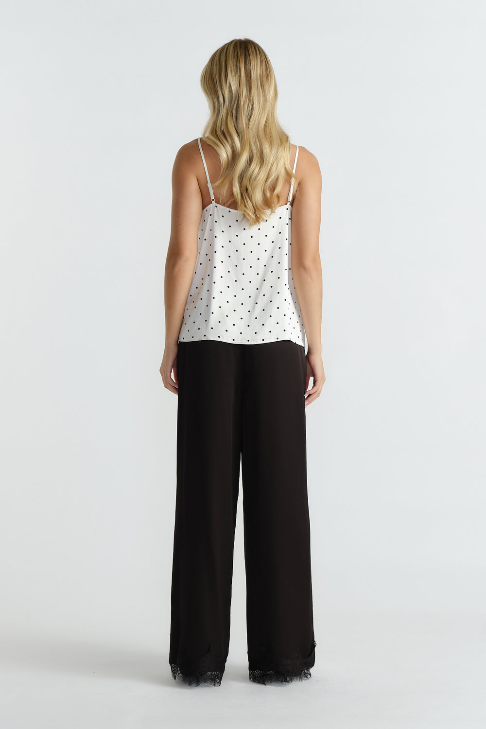 Woman wearing ivory spot camisole with delicate straps paired with wide-leg black pants featuring lace trim hem.