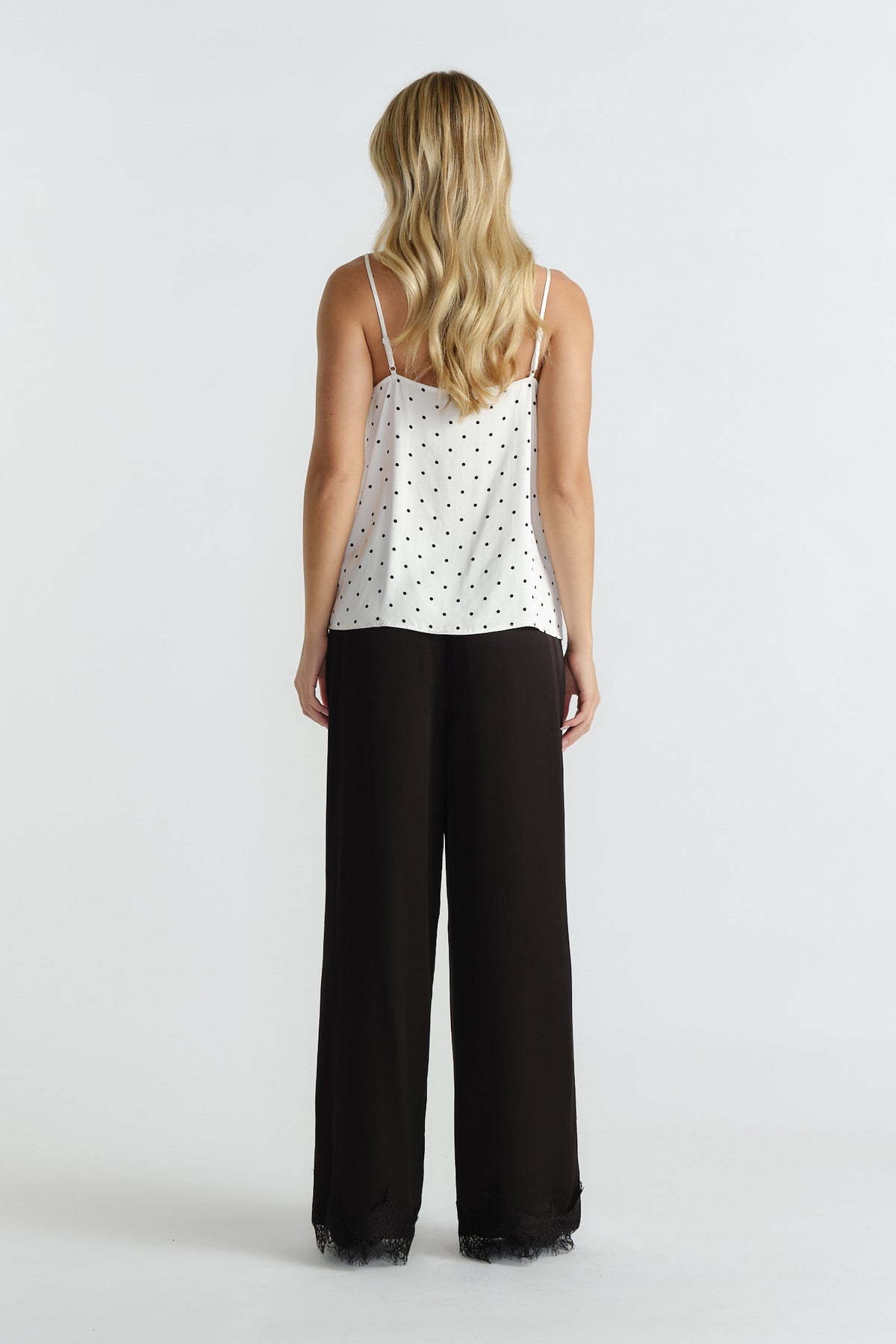 Woman wearing ivory spot camisole with delicate straps paired with wide-leg black pants featuring lace trim hem.