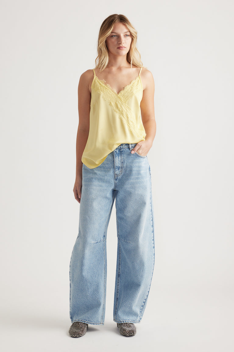 Woman wearing a soft yellow lace-trimmed cami with relaxed light-wash wide-leg jeans and patterned shoes