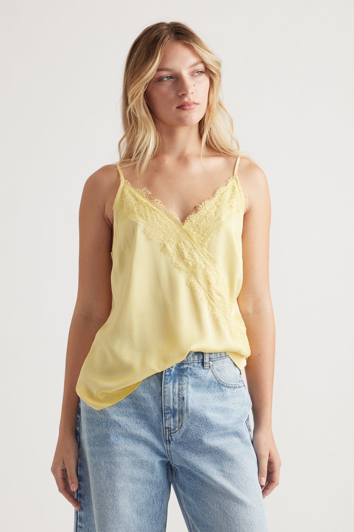 Woman wearing a soft yellow lace-trimmed cami paired with relaxed light-wash denim jeans for a casual look
