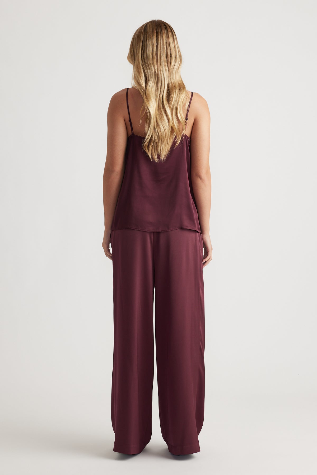 Woman wearing a plum satin camisole with thin straps paired with matching wide-leg satin pants for a sleek look