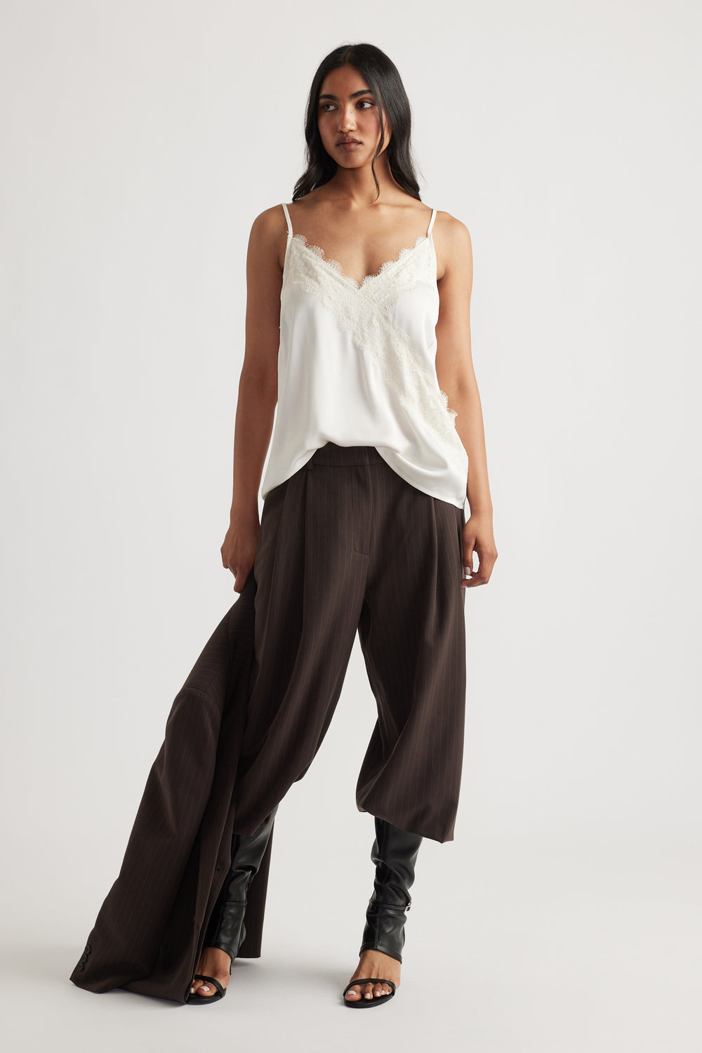 Woman wearing a delicate ivory lace-trimmed cami paired with wide-leg chocolate brown trousers and black heeled boots