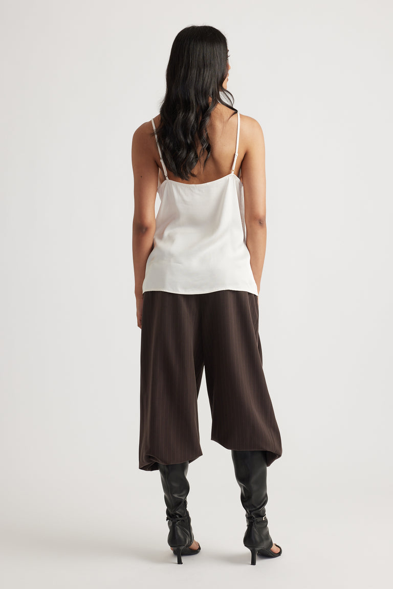 Woman wearing a vanilla lace cami paired with loose dark brown pants and slouchy black heeled boots for chic layering