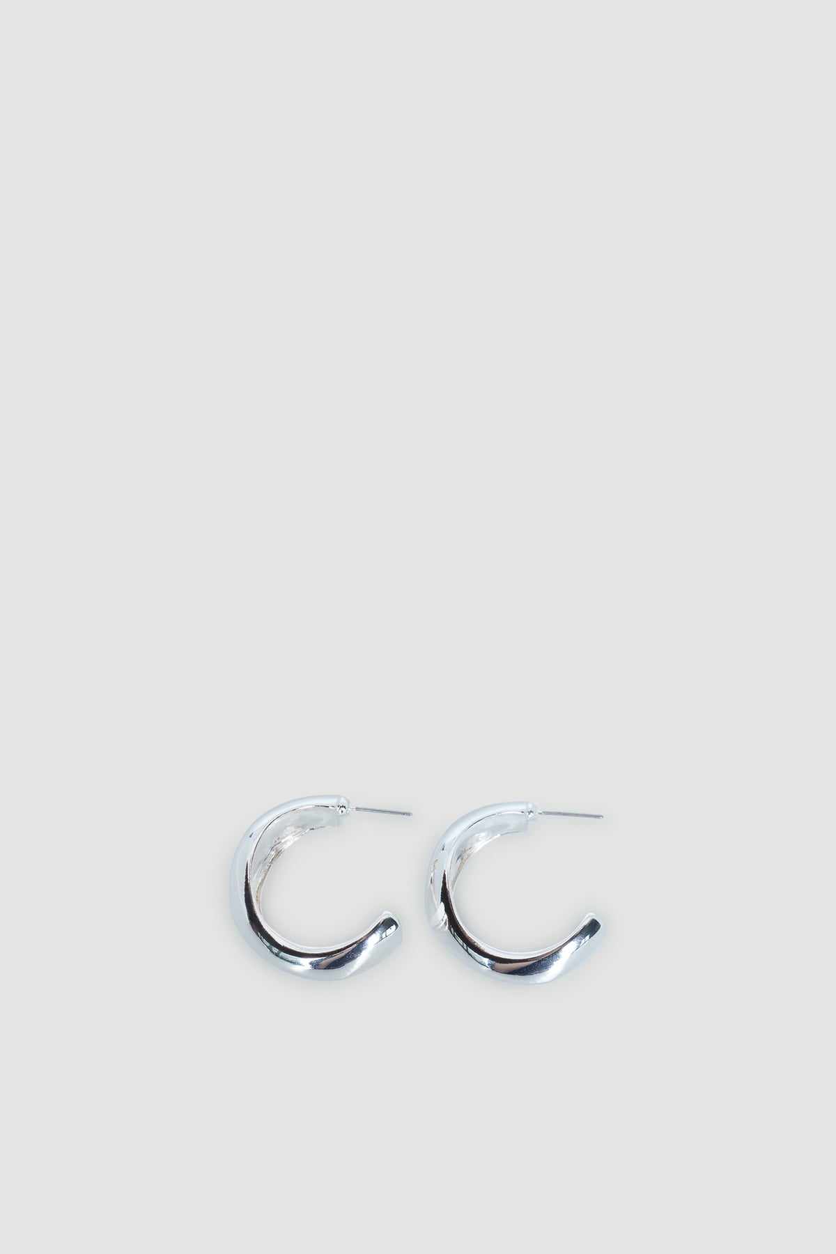 Pair of polished silver hoop earrings with an abstract, slightly chunky curved design on a light background.