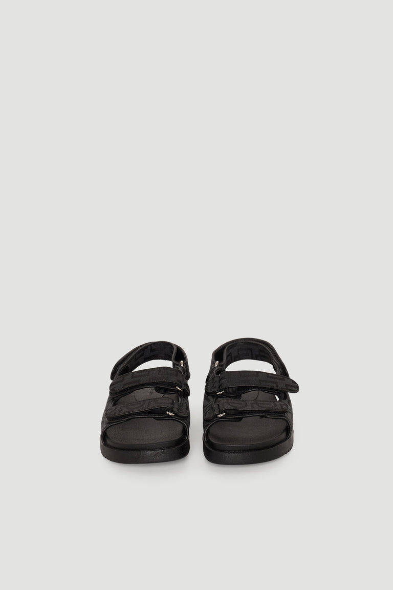 Pair of black sandals featuring adjustable straps and chunky soles with subtle monogram detailing for everyday wear.