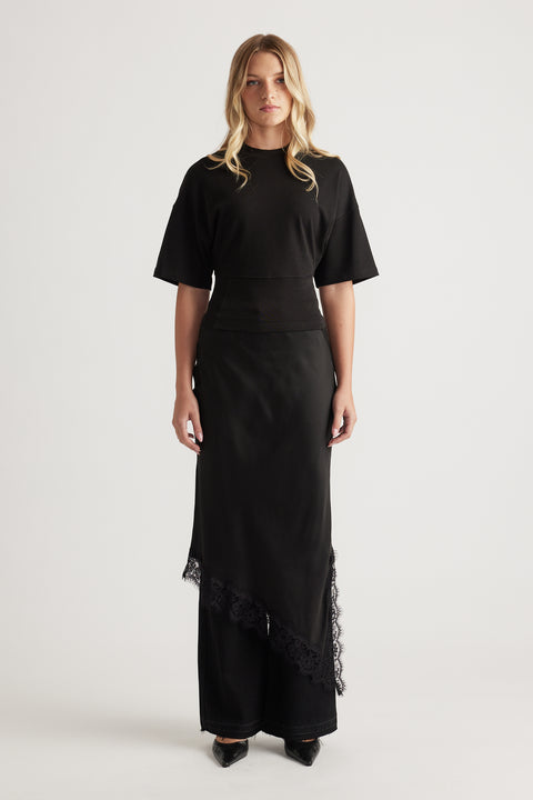Woman wearing a black fitted waist tee paired with a long asymmetrical skirt featuring lace trim and pointed black shoes