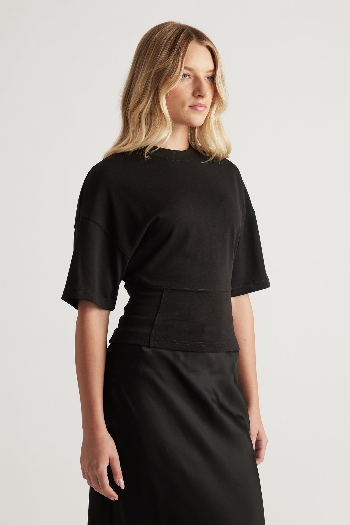 Woman in a black fitted waist tee with short sleeves paired with a sleek black skirt for a polished look