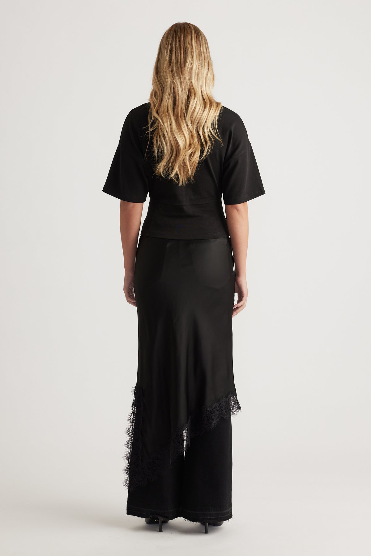 Back view of woman wearing a fitted black tee with wide sleeves paired with a sleek black skirt featuring lace trim detailing