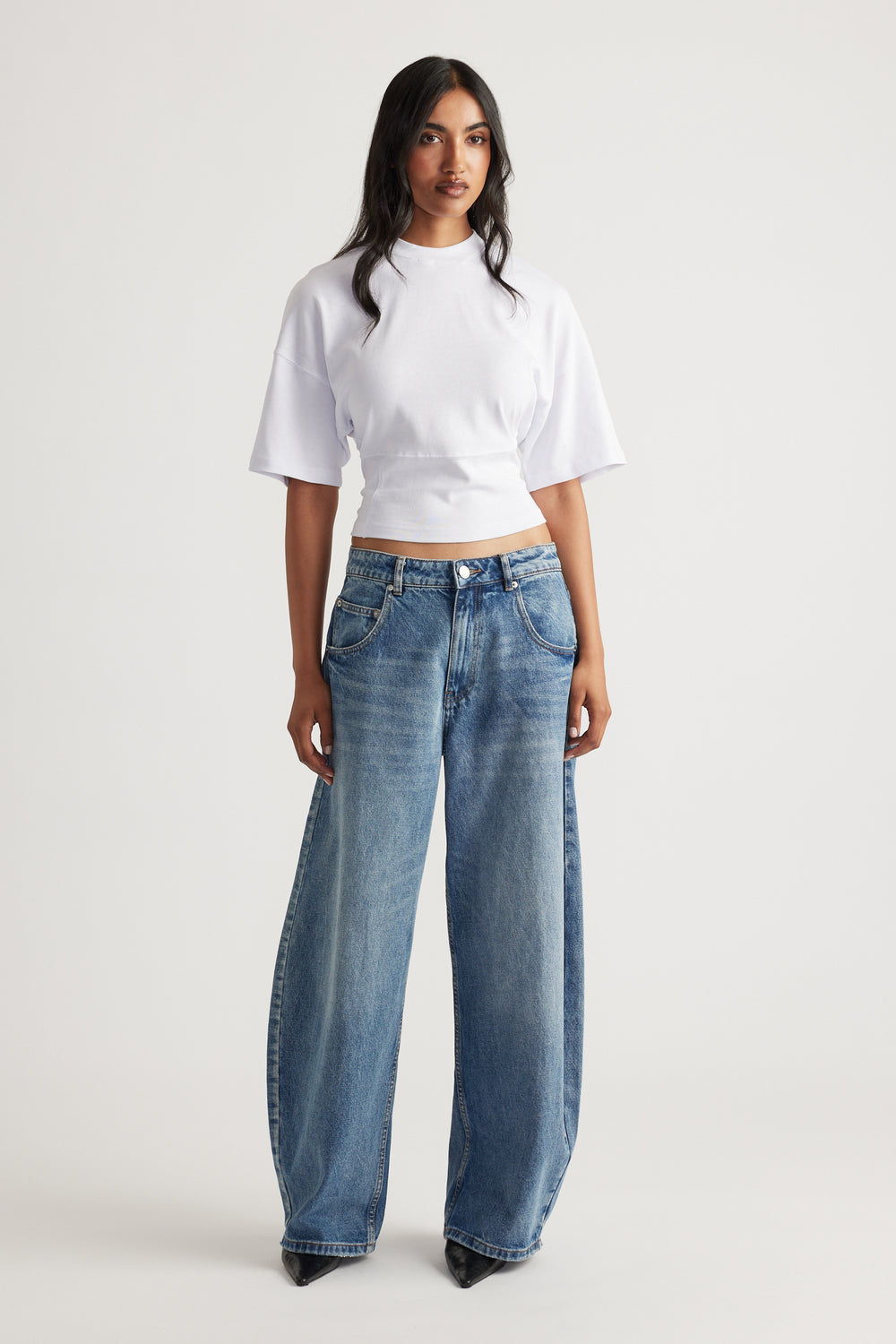 Woman wearing a bright white fitted waist tee paired with loose wide-leg blue denim jeans and black pointed shoes