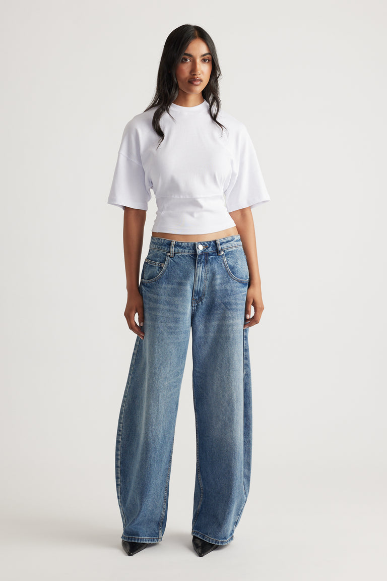 Woman wearing a bright white fitted waist tee paired with loose wide-leg blue denim jeans and black pointed shoes