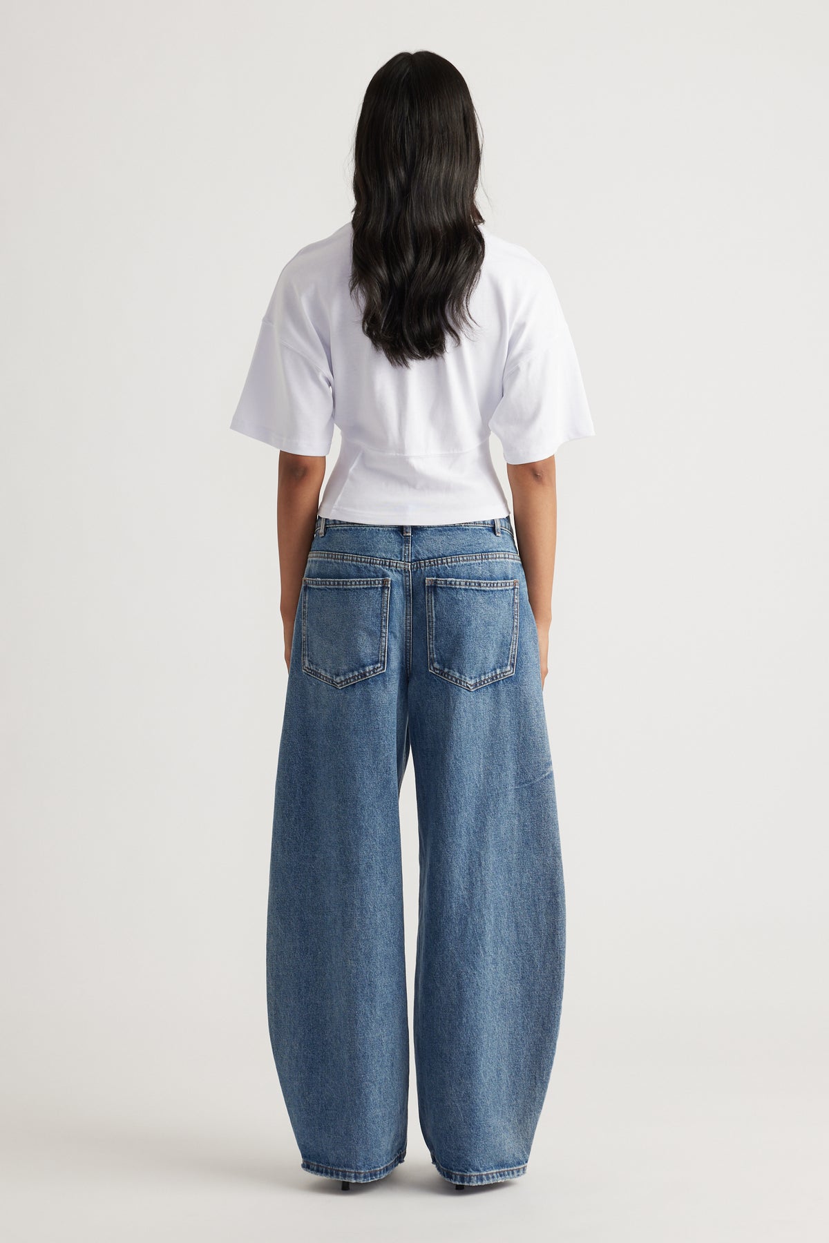 Back view of woman wearing wide-leg blue denim jeans paired with a white fitted short-sleeve top
