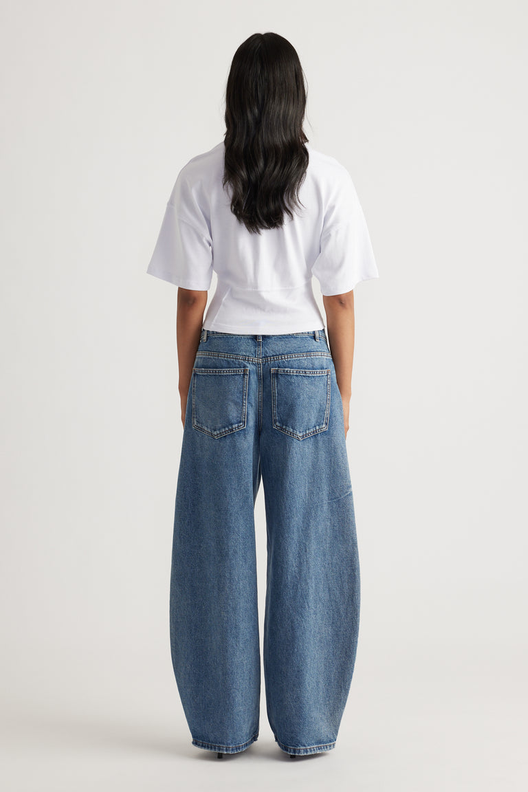 Back view of woman wearing wide-leg blue denim jeans paired with a white fitted short-sleeve top