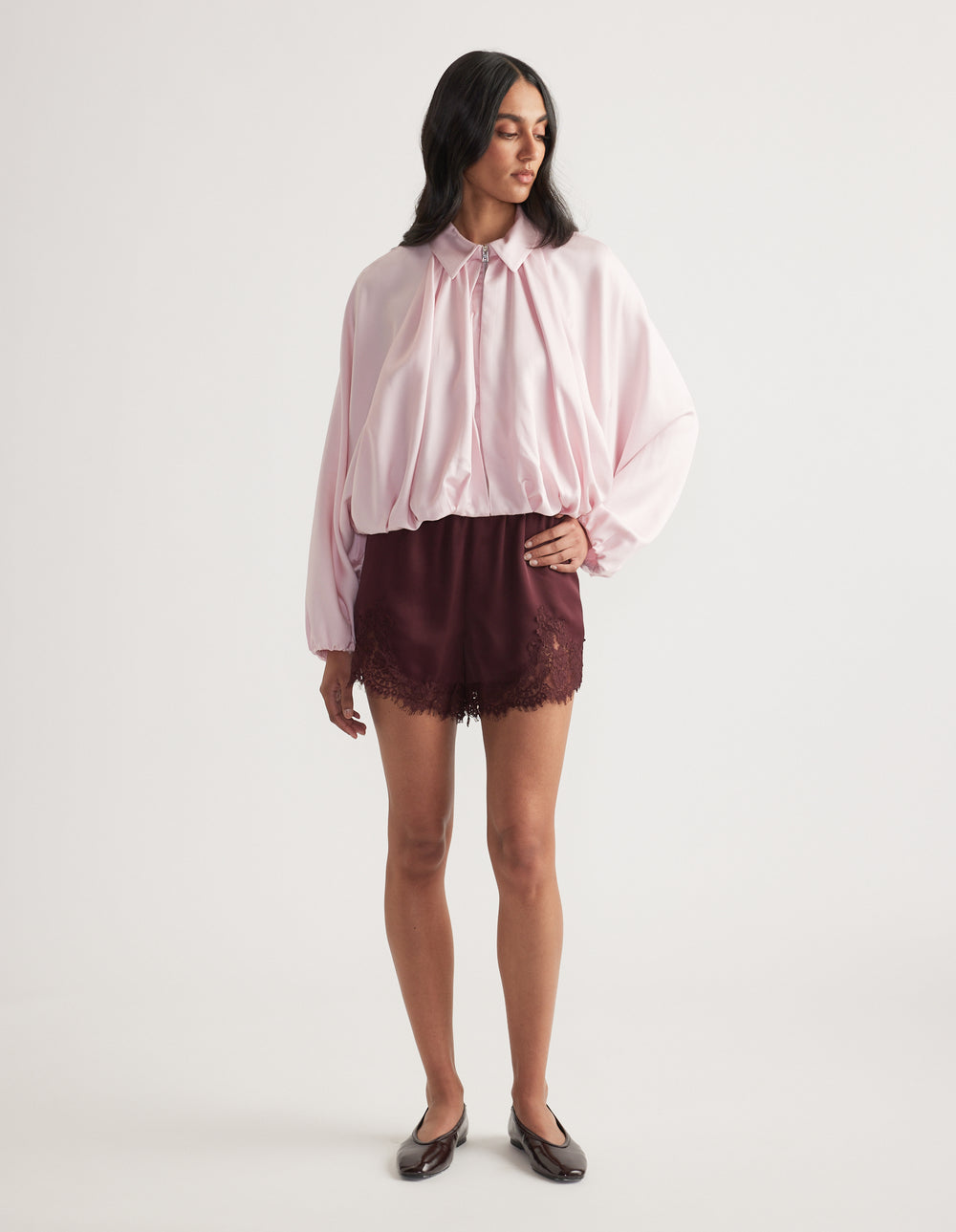 Woman wearing a billowy pale pink blouse with burgundy lace trim shorts and black ballet flats