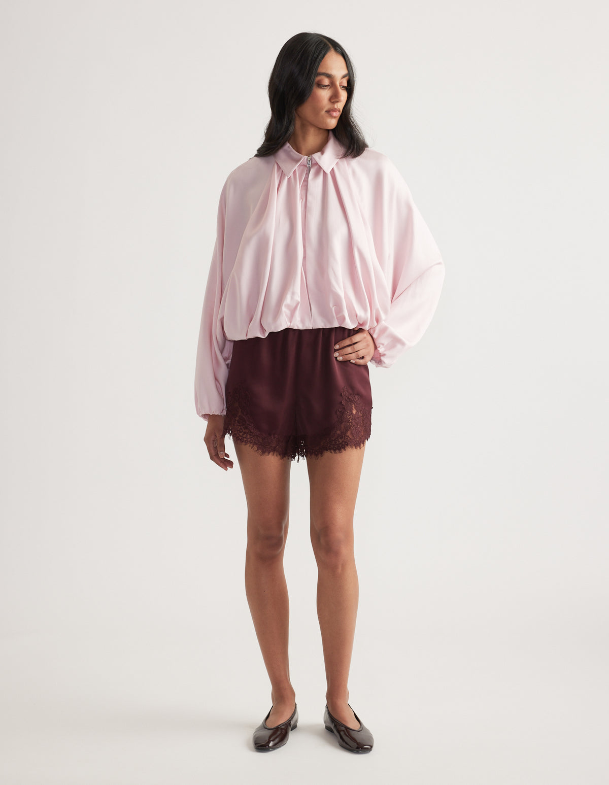 Woman wearing a billowy pale pink blouse with burgundy lace trim shorts and black ballet flats