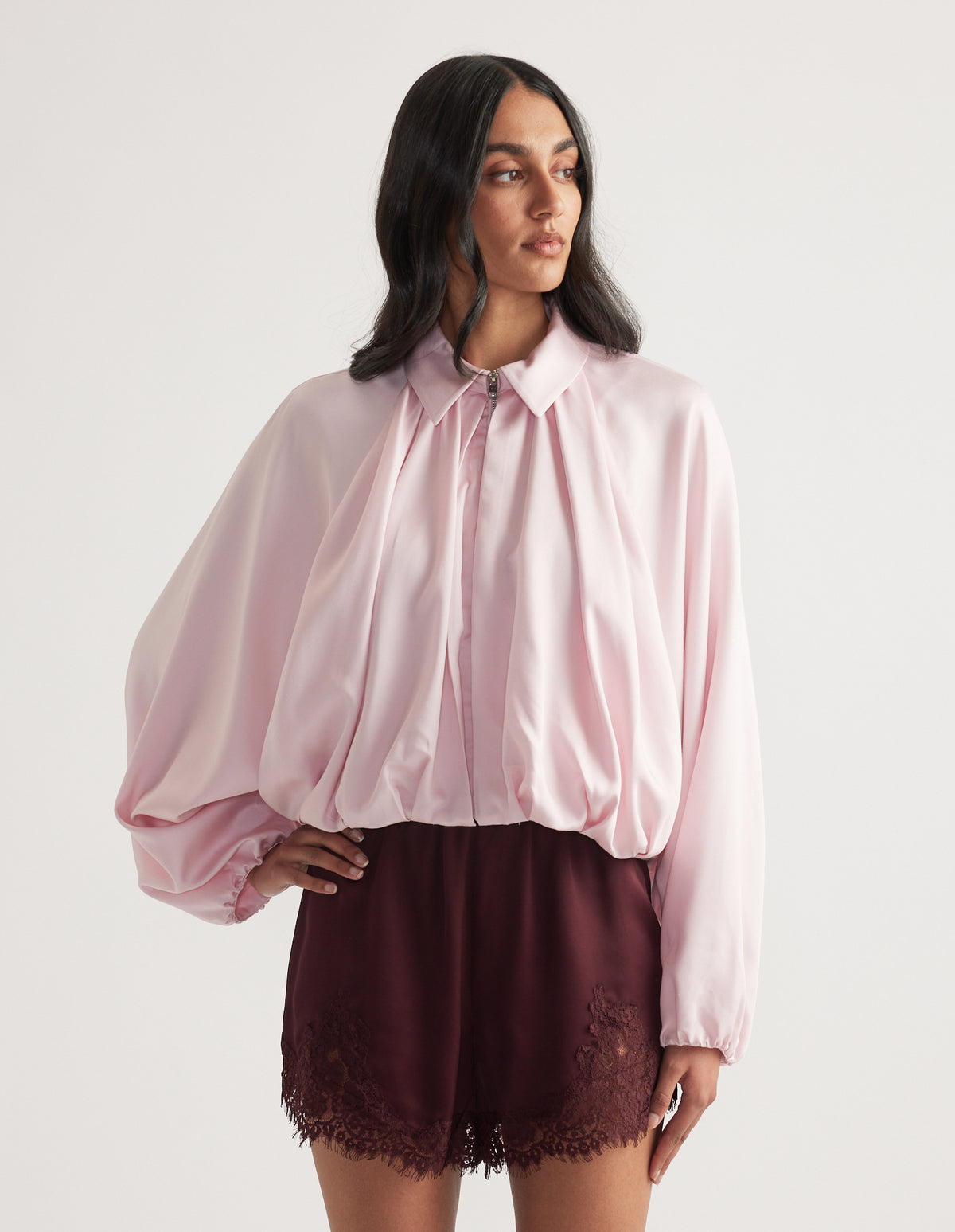 Woman wearing a light pink collared jacket with puffed sleeves and burgundy lace-trim shorts