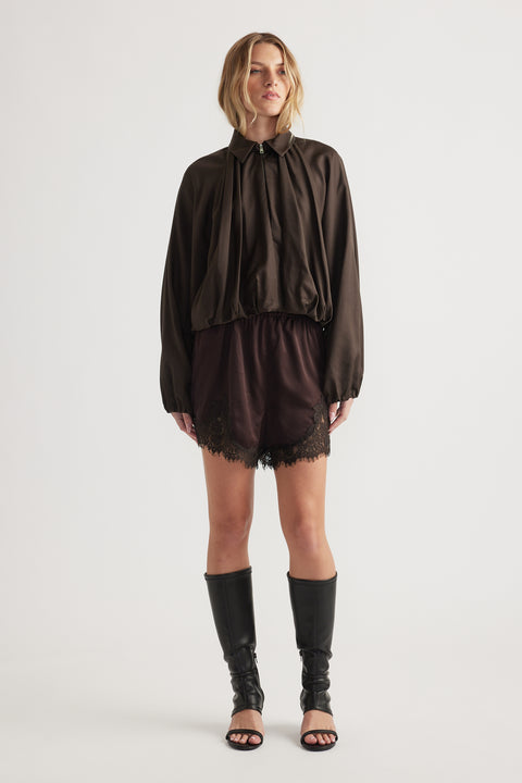 Woman wearing a relaxed fit dark puffed sleeve jacket paired with black lace-trimmed shorts and tall black boots