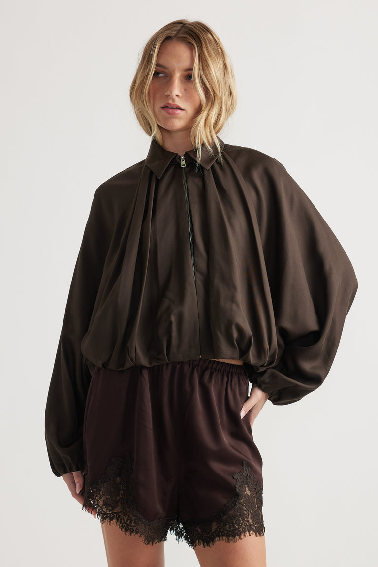 Woman wearing a dark puffed sleeve jacket with zip front paired with silky shorts featuring lace trim on hem