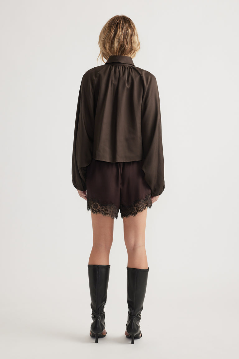 Woman wearing a loose dark long-sleeve top paired with black lace-trimmed shorts and knee-high boots, back view