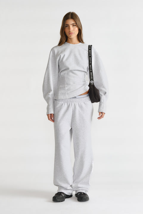 Woman wearing light grey cinched sweatshirt and matching relaxed sweatpants, styled with black shoes and a black shoulder bag