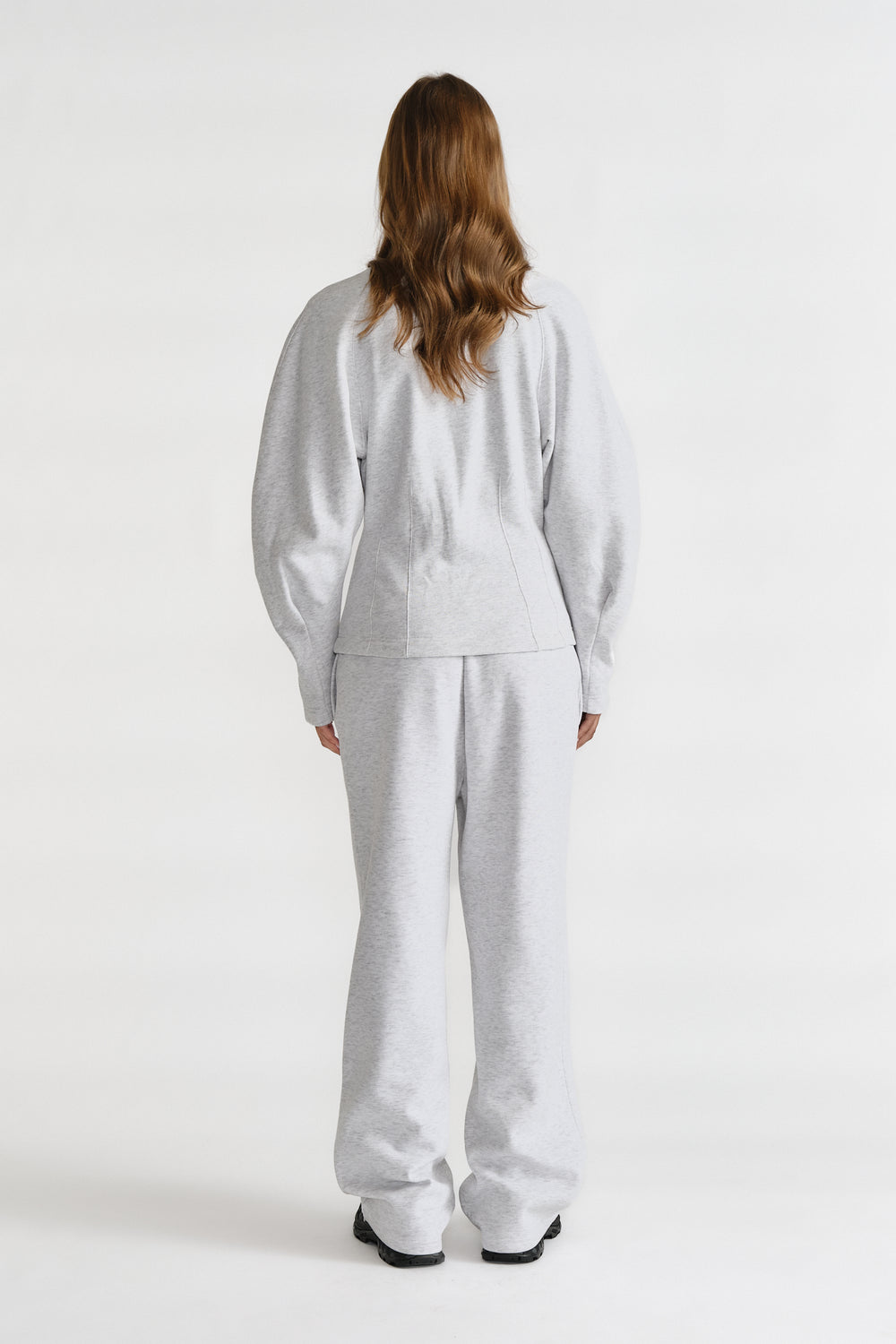 Rear view of a woman wearing light grey cinched sweatshirt and matching wide-leg sweatpants with black shoes
