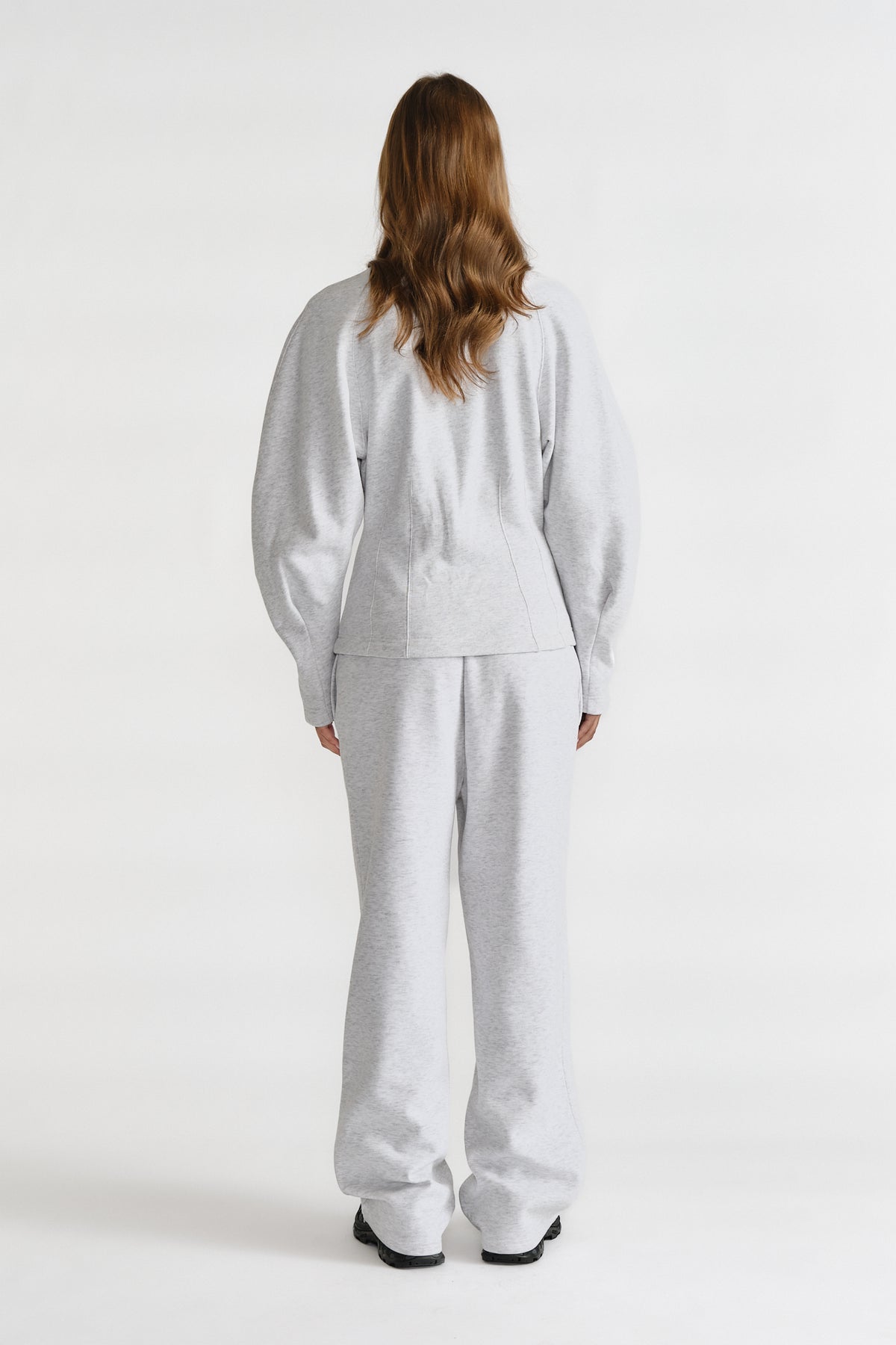 Rear view of a woman wearing light grey cinched sweatshirt and matching wide-leg sweatpants with black shoes