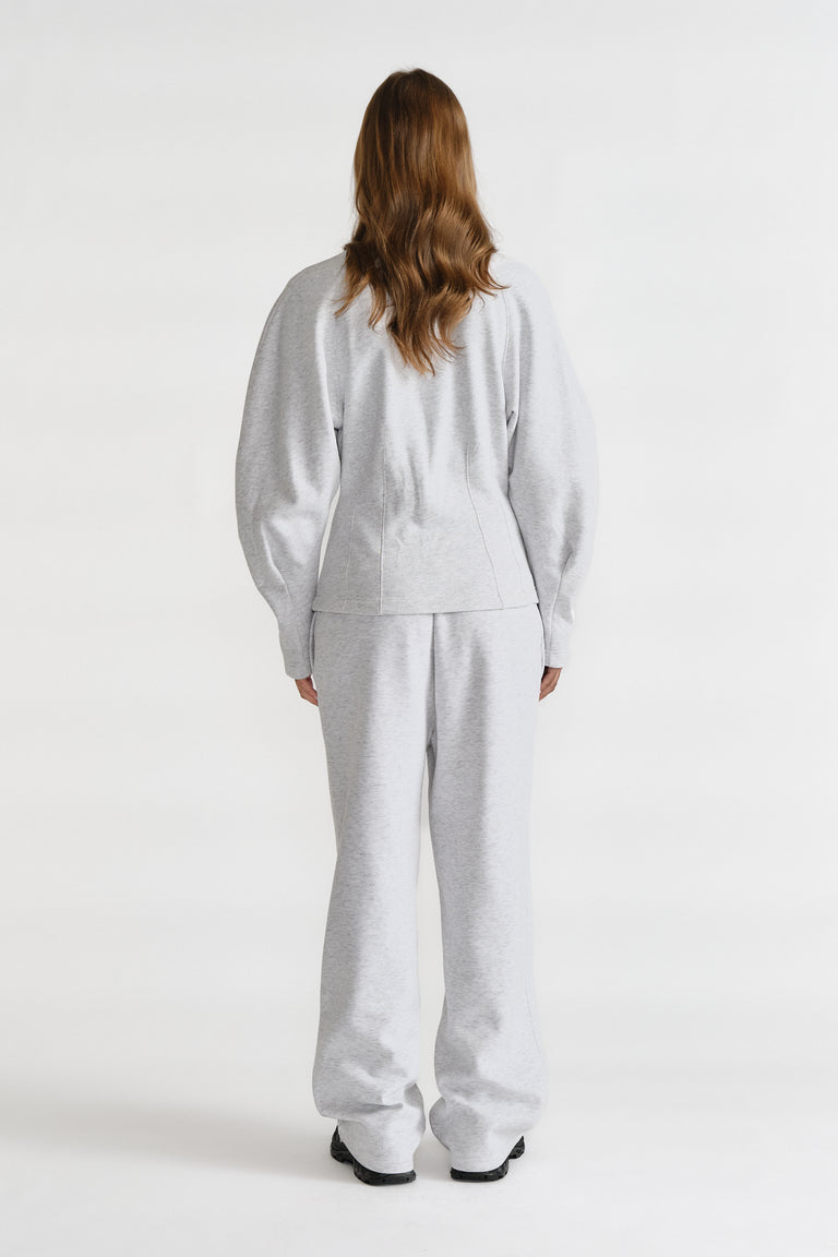 Rear view of a woman wearing light grey cinched sweatshirt and matching wide-leg sweatpants with black shoes